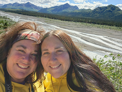 Stacey with her sister smiling in front of some mountains.