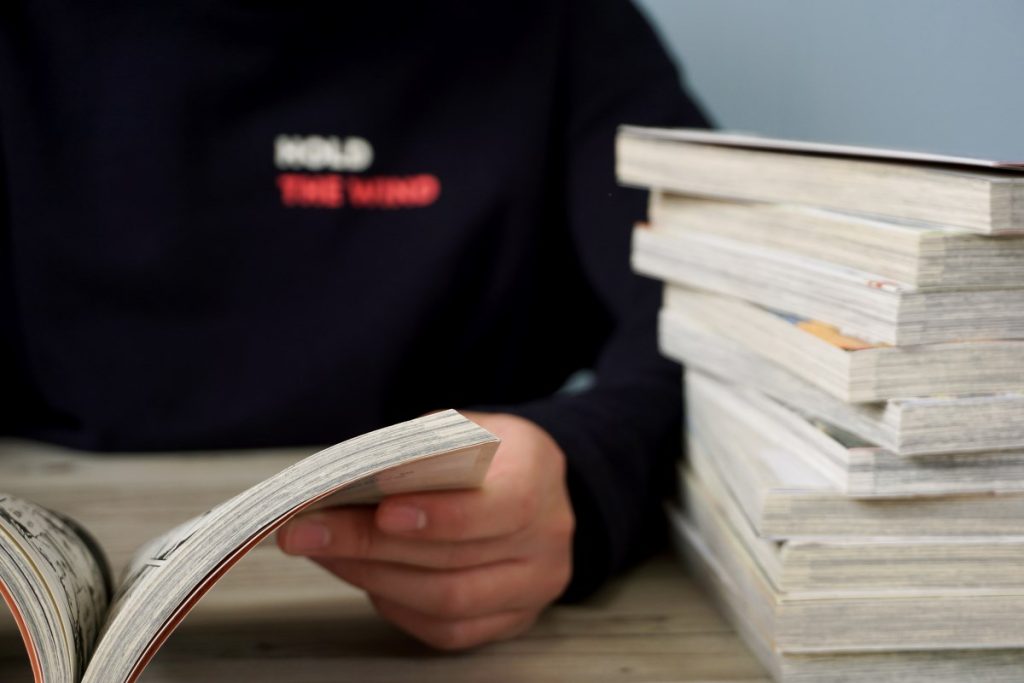 A man reading a graphic novel with a stack of books next to him